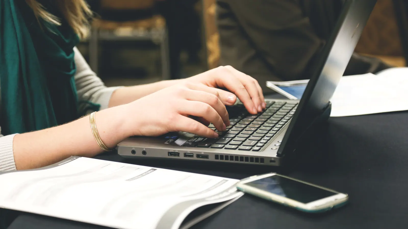 Person typing on a laptop next to a smartphone